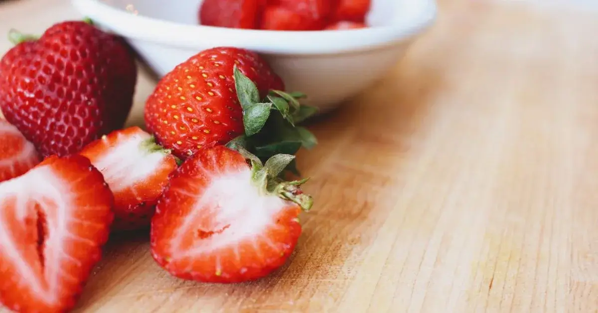 Several strawberries, cut in half, on a wooden cutting board